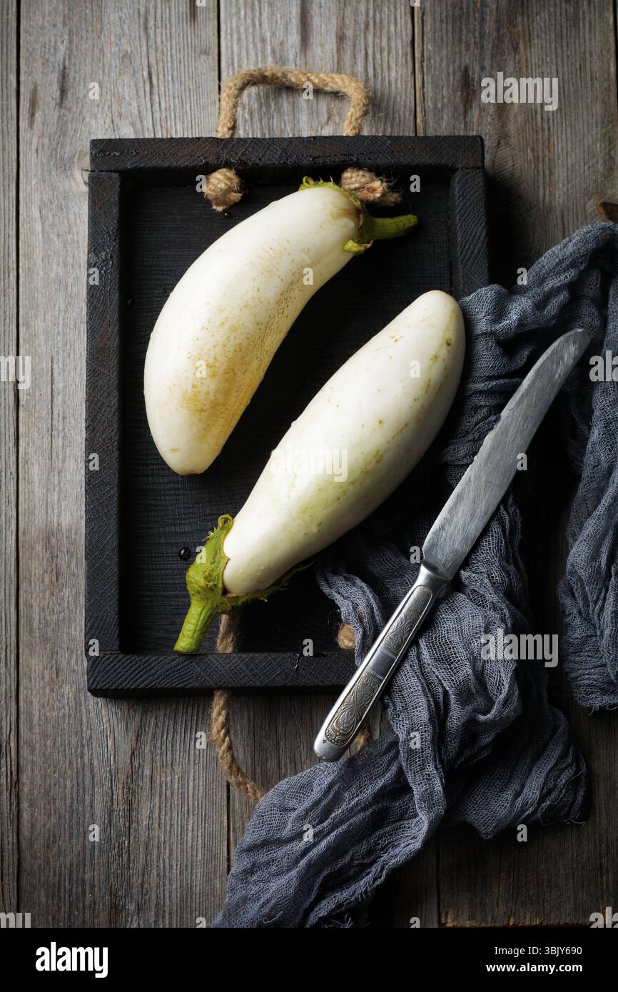 Two fresh white eggplants in a vintage box on an old wooden background Selective focus. Top view. Copy space Stock Photo