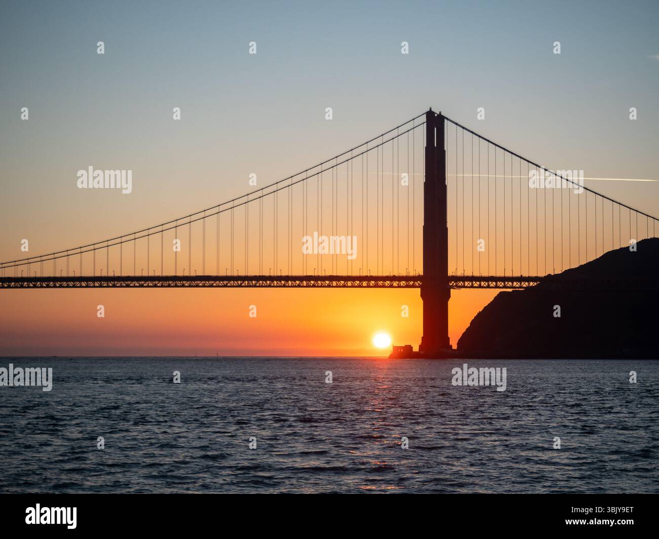 The Golden Gate Bridge is silhouetted against the setting sun, creating ...