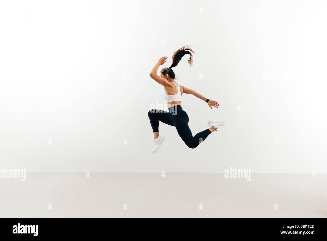 Side view of woman with muscular body jumping against white wall Stock Photo