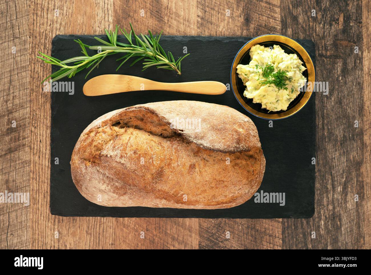 Freshly baked bread and rustic handmade herbs butter on the table. Stock Photo