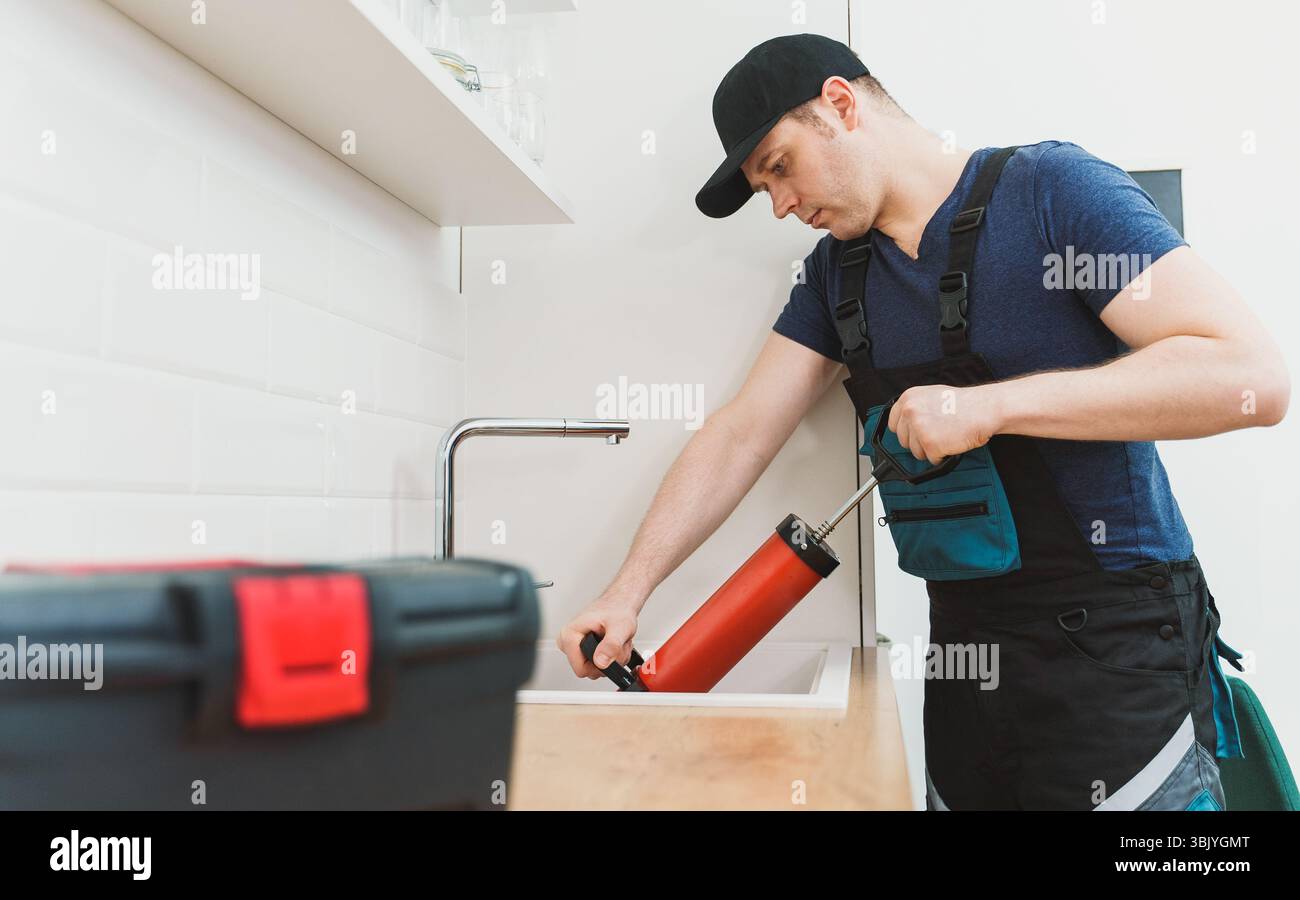 Plumber unclogging kitchen sink with professional force pump cleaner. Stock Photo