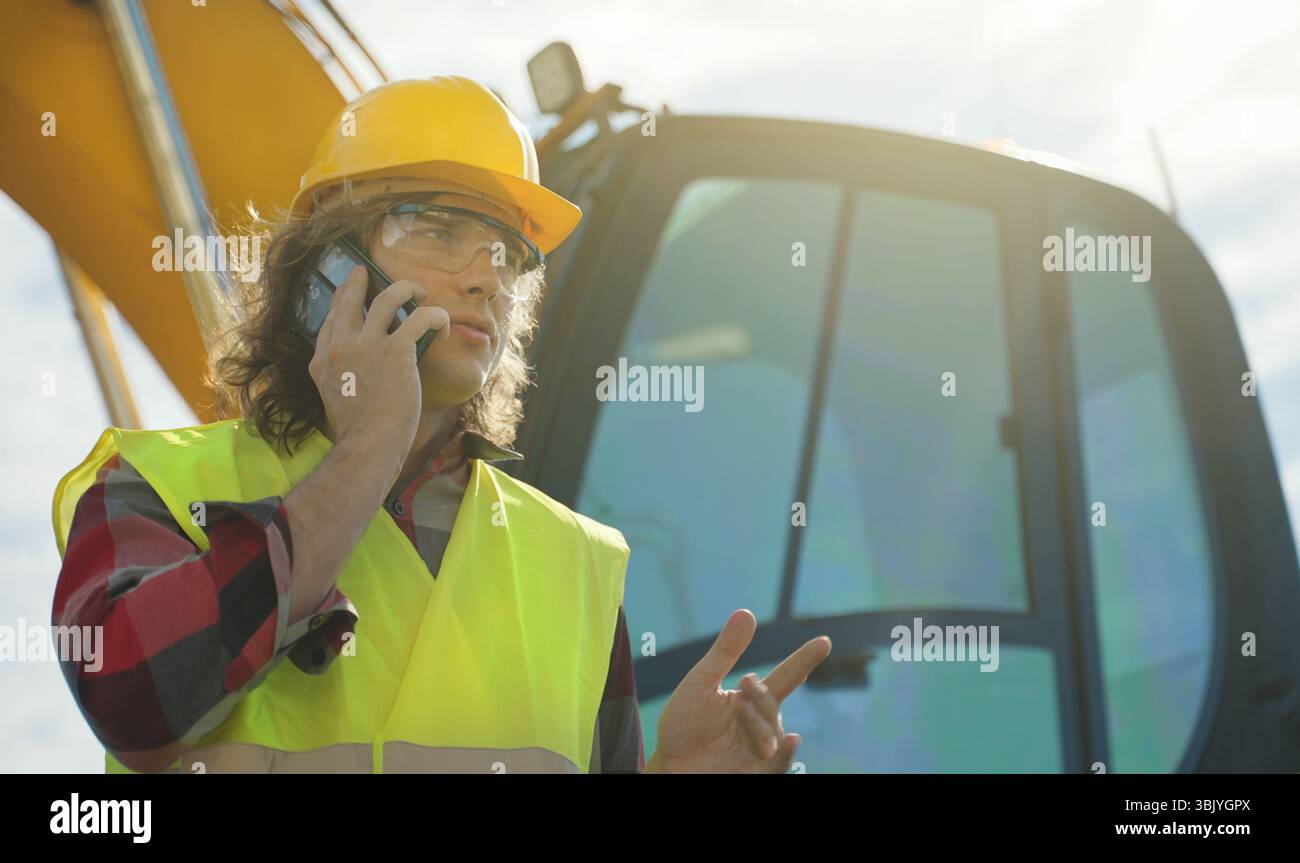 Excavator operator in hard hat talking by smartphone. Stock Photo