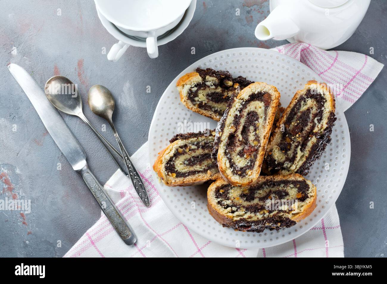 Pieces honey roll with poppy seeds and raisins on a white platen on gray concrete background. Selective focus. Top view. Place f Stock Photo