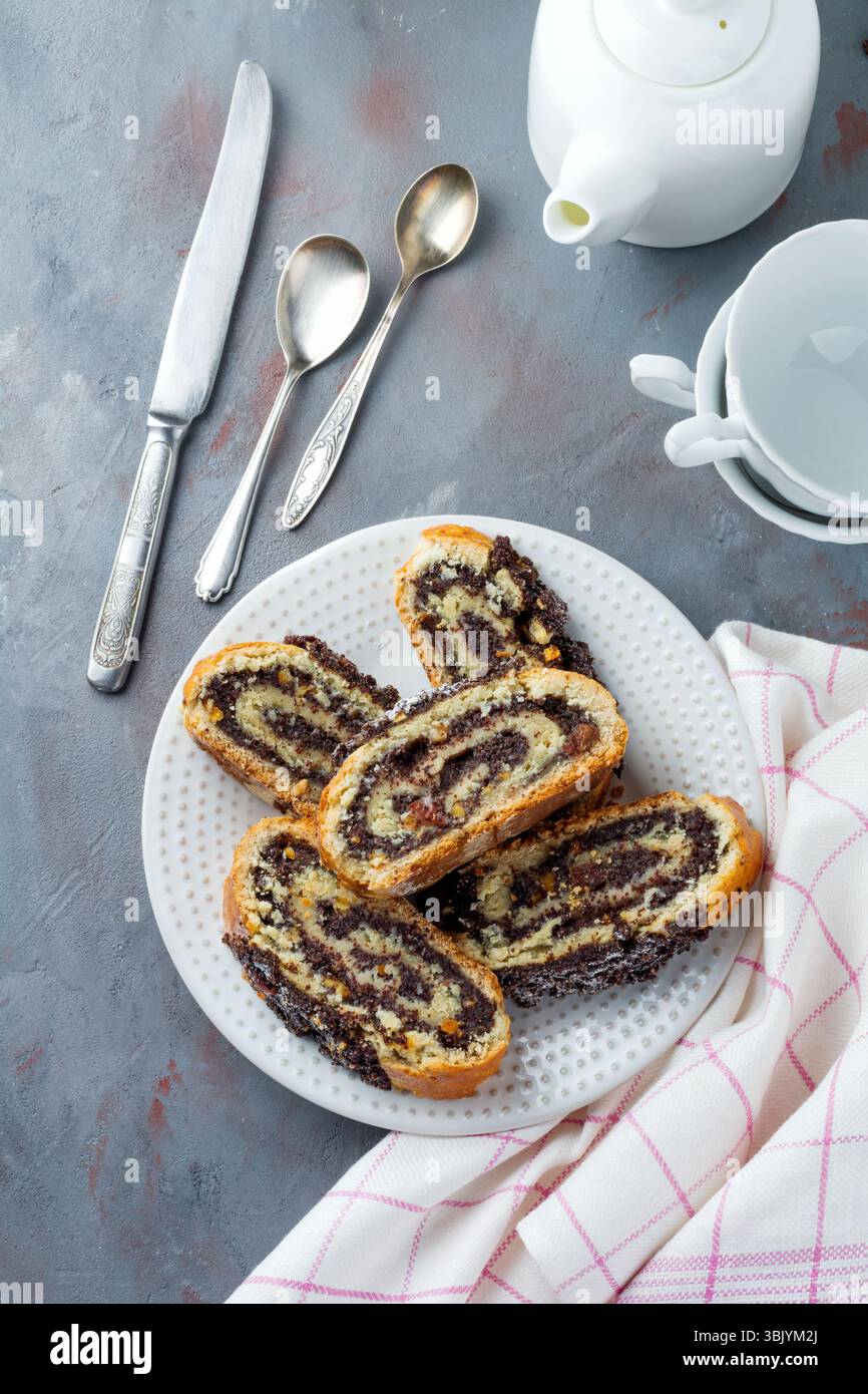 Pieces honey roll with poppy seeds and raisins on a white platen on gray concrete background. Selective focus. Top view. Place f Stock Photo