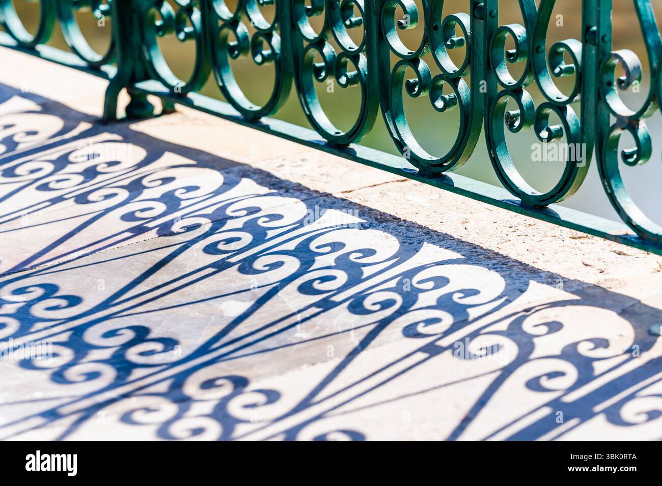 Sunlight creates intricate shadows of a green wrought iron railing on ...