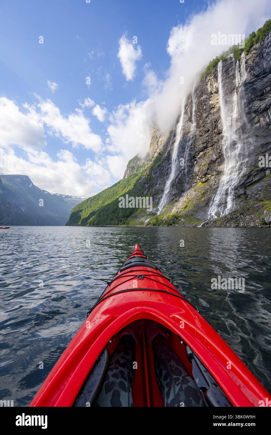 Kayak trip on the Geirangerfjord at the waterfall The Seven Sisters, tip of a red kayak in the fjord, atmospheric fjord landscape, first person view, Stock Photo