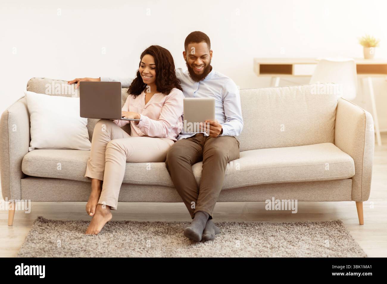 African american couple sitting on couch, using laptop and tablet Stock ...