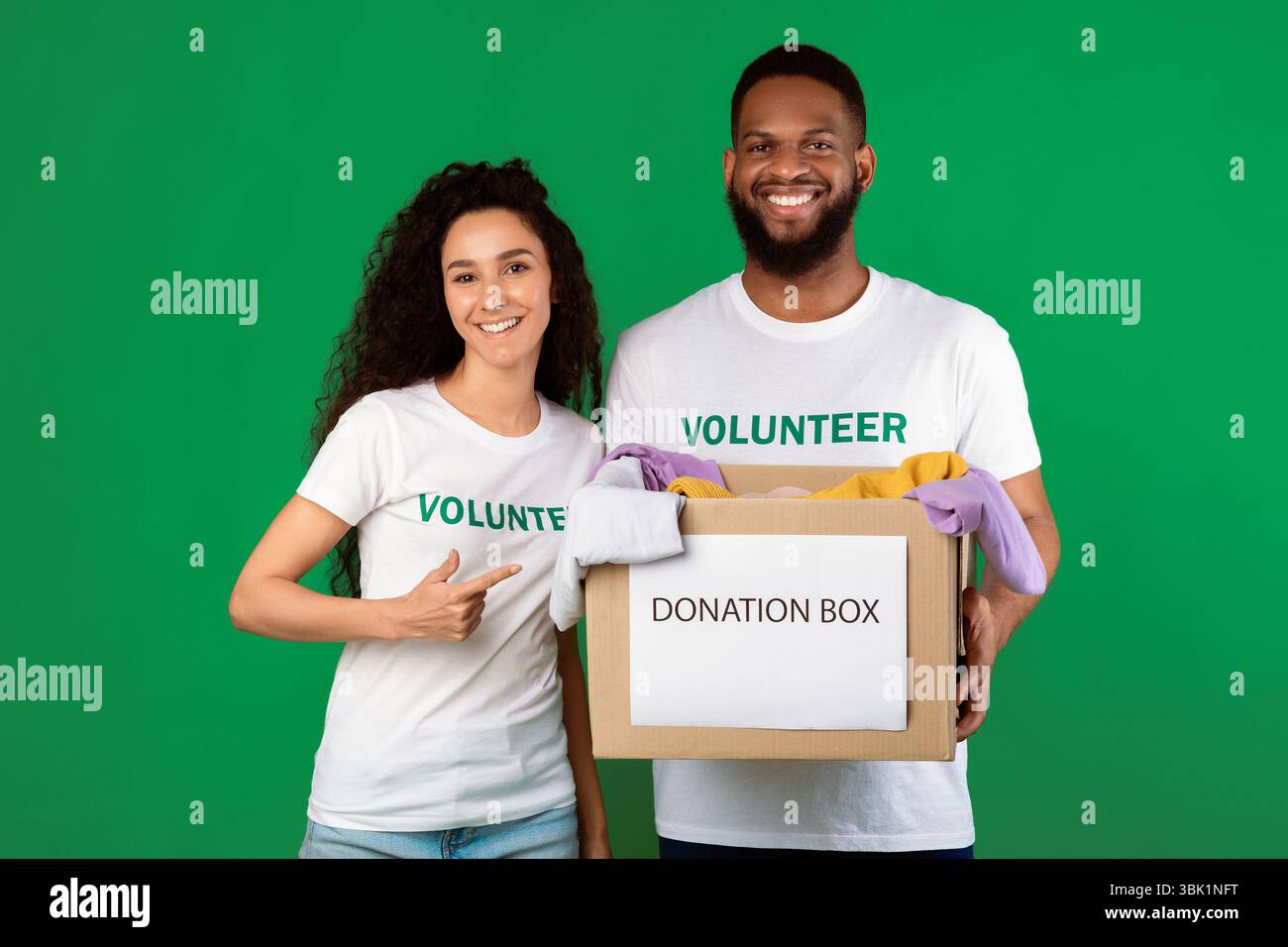 Two Volunteers Holding Donation Box Standing Over Green Background Stock Photo