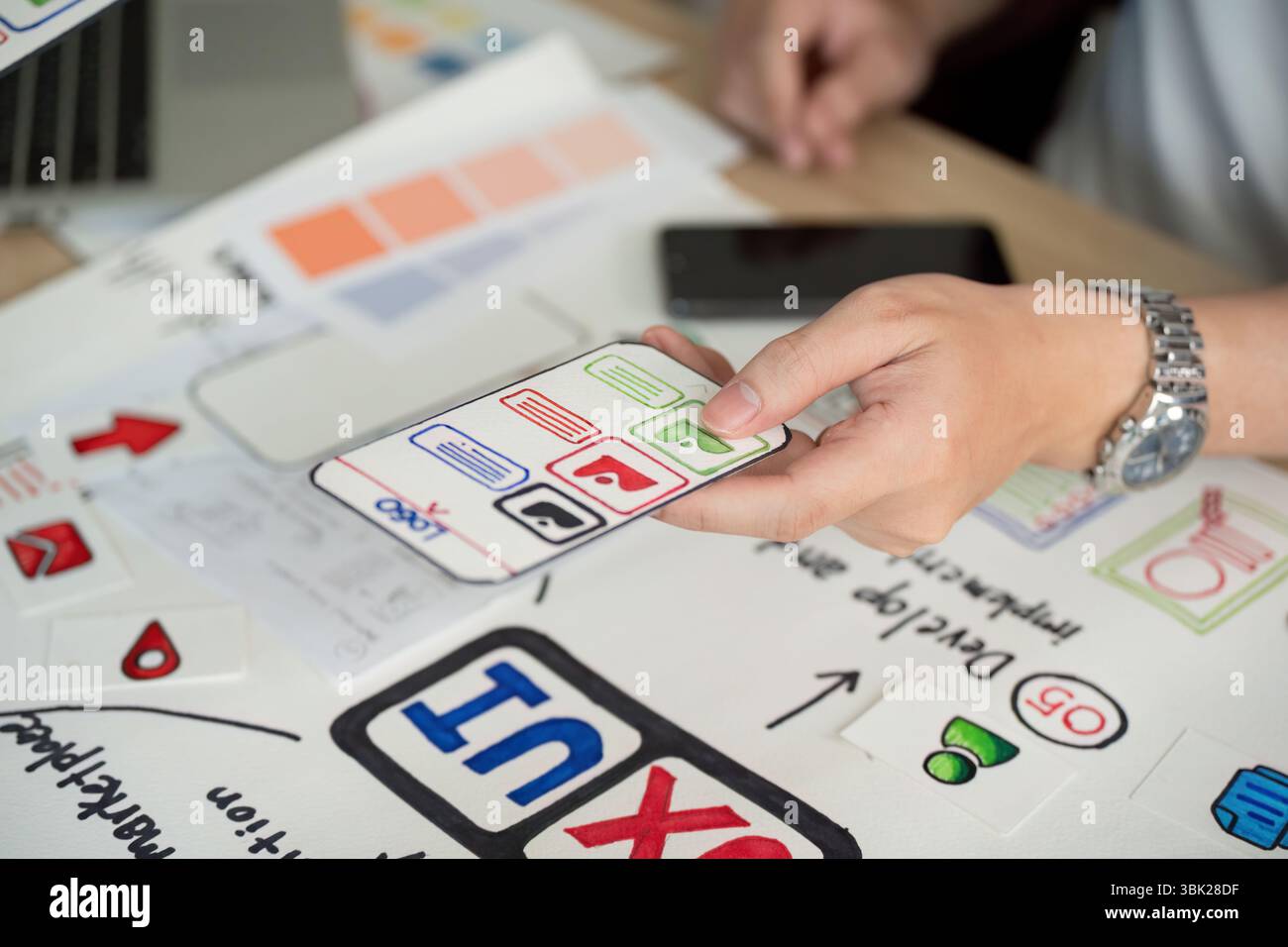 User Interface Design. Hand holding smartphone with app features during brainstorming session. Stock Photo