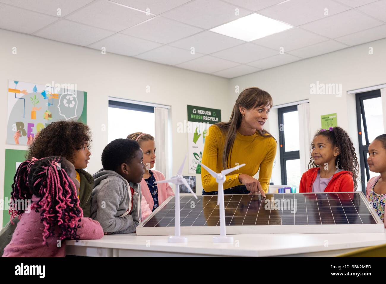 Female teacher engaging diverse students with solar panel in eco ...