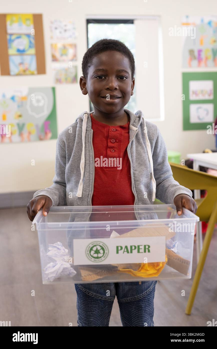 In school, african american boy holding recycling bin, learning about environmental responsibility Stock Photo