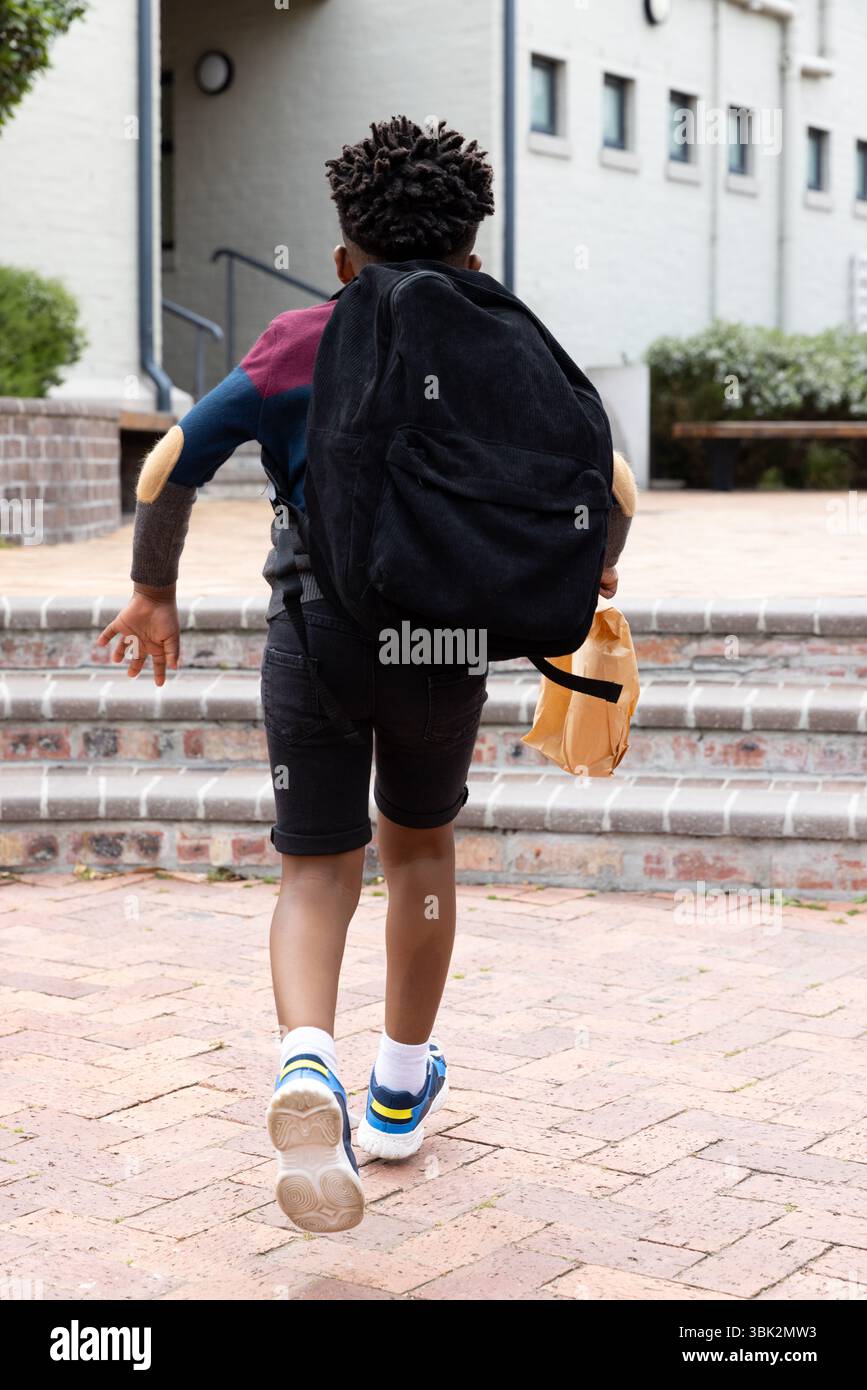 African american boy with backpack running up steps to school, holding ...