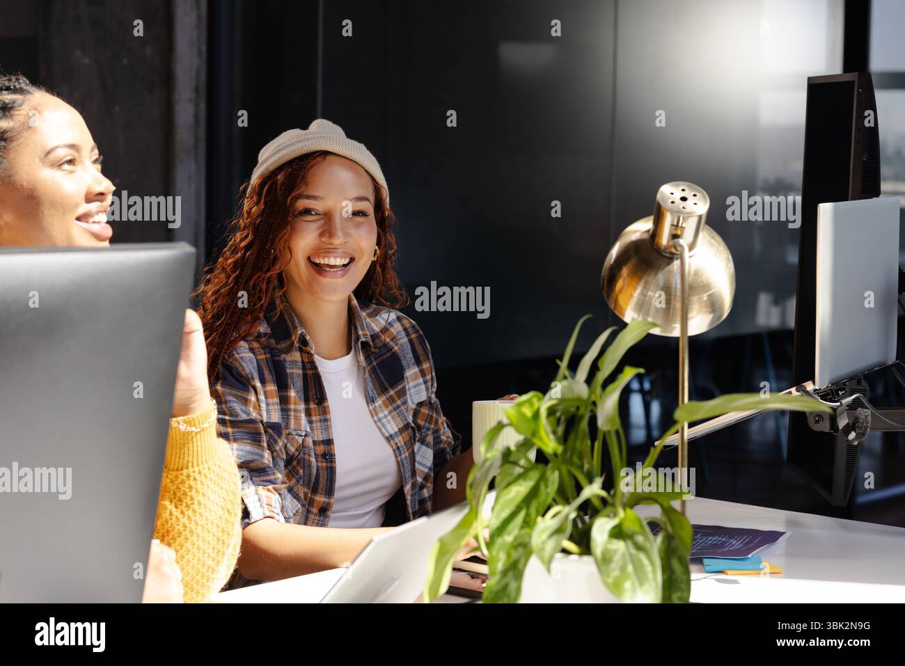 Diverse women collaborating on coding project at modern office, smiling and engaged Stock Photo