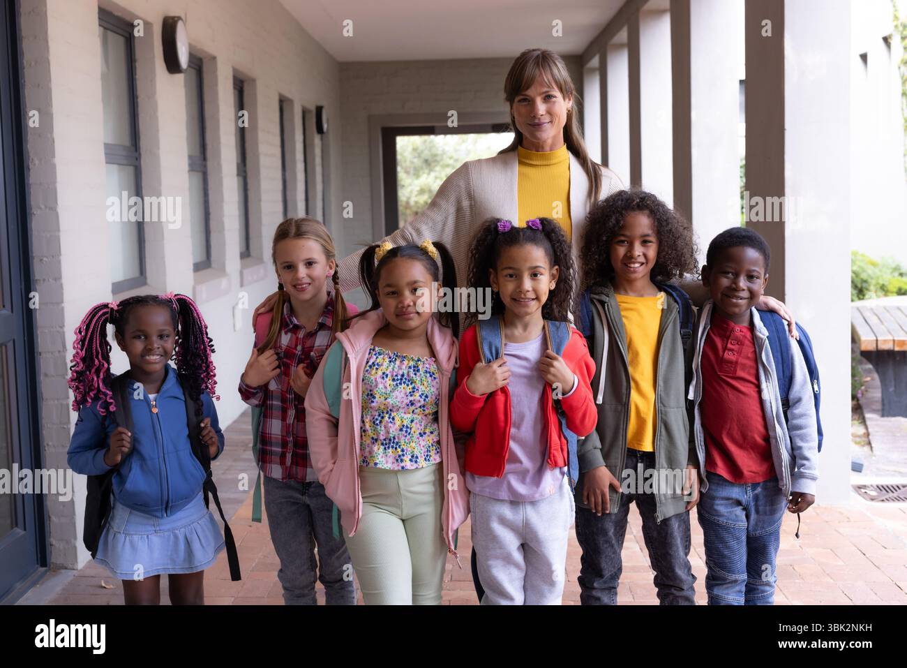 Smiling female teacher with diverse group of children wearing backpacks ...