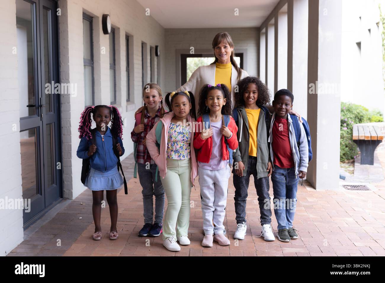 Female teacher with diverse group of smiling children standing together ...