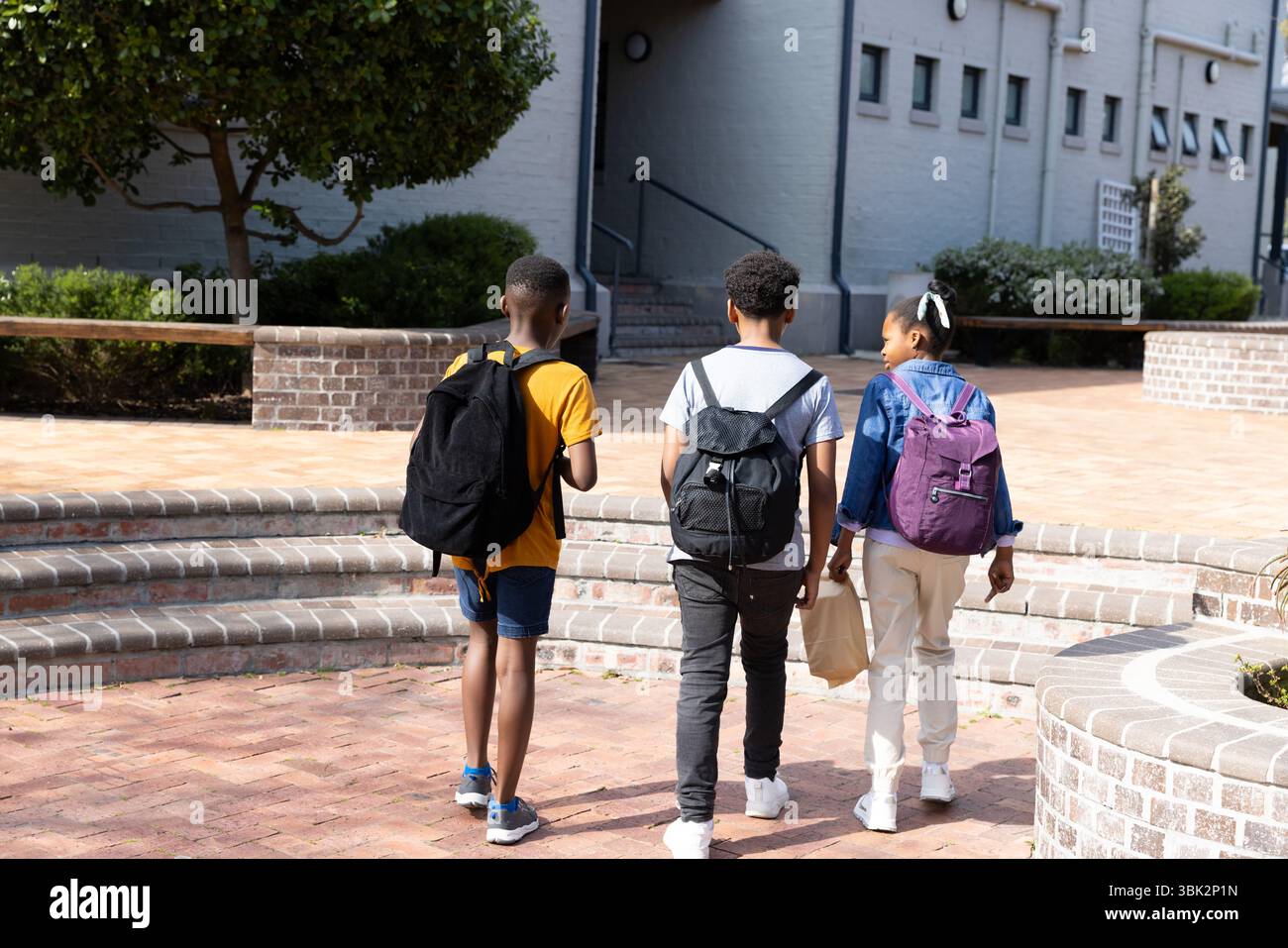 diverse students walking together on school campus with backpacks Stock Photo