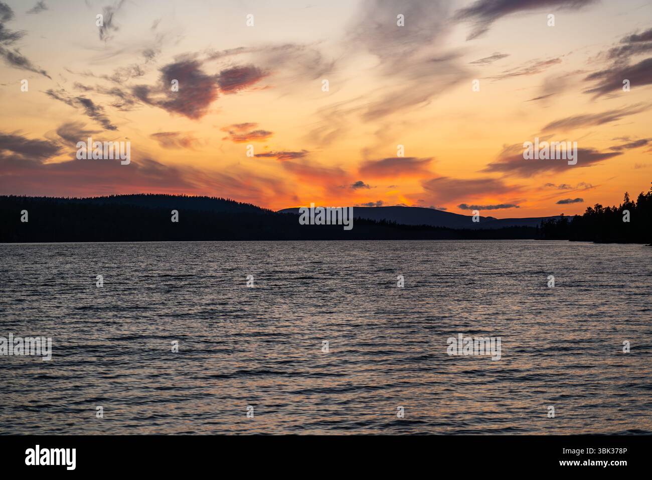 As the sun sets, vibrant colors reflect on Hällsjön lake, surrounded by ...