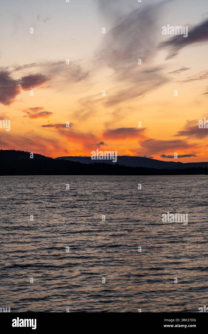 As the sun sets, vibrant colors reflect on Hällsjön lake, surrounded by ...