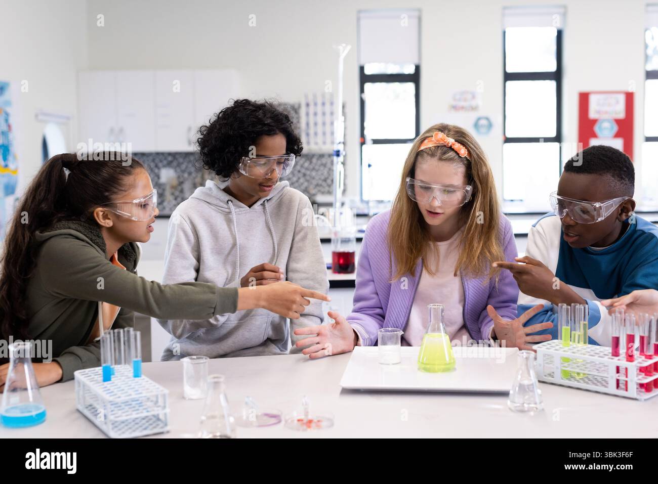 Diverse students in science class discussing experiment with test tubes and beakers, at school Stock Photo