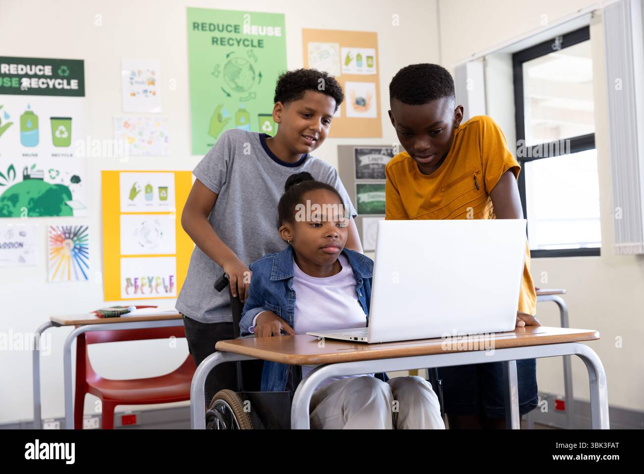 Diverse students collaborating on laptop in classroom, engaged in recycling project, at school Stock Photo