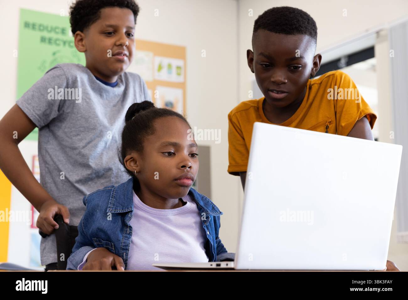 Diverse students collaborating on laptop in classroom, focused on group project, at school Stock Photo