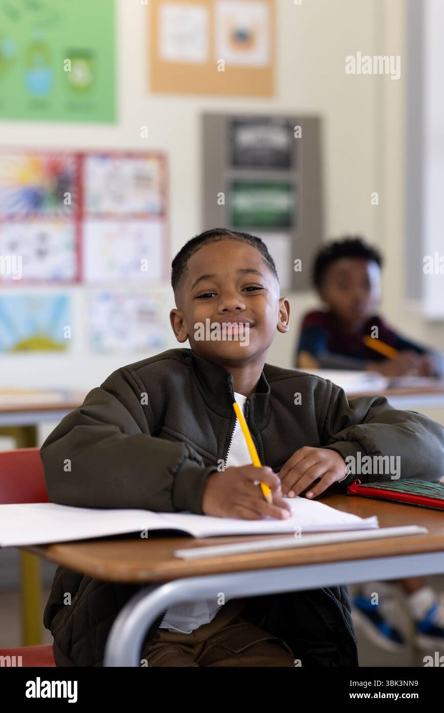 Smiling african american boy writing in classroom, enjoying school activities with classmates Stock Photo