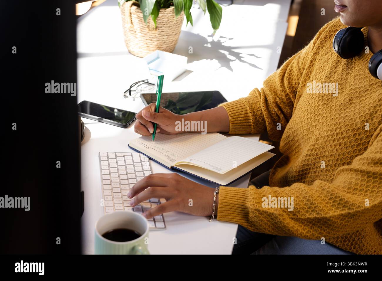 Woman coding at desk, writing notes in notebook, focused on work, at office Stock Photo