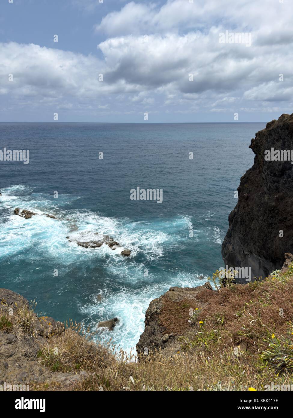 Vertical shoot of ocean waves crash against rocky coastline of Madeira, Portugal. The seascape features white surf, sea spray, and rugged stones. - Smartphone Captured Stock Image