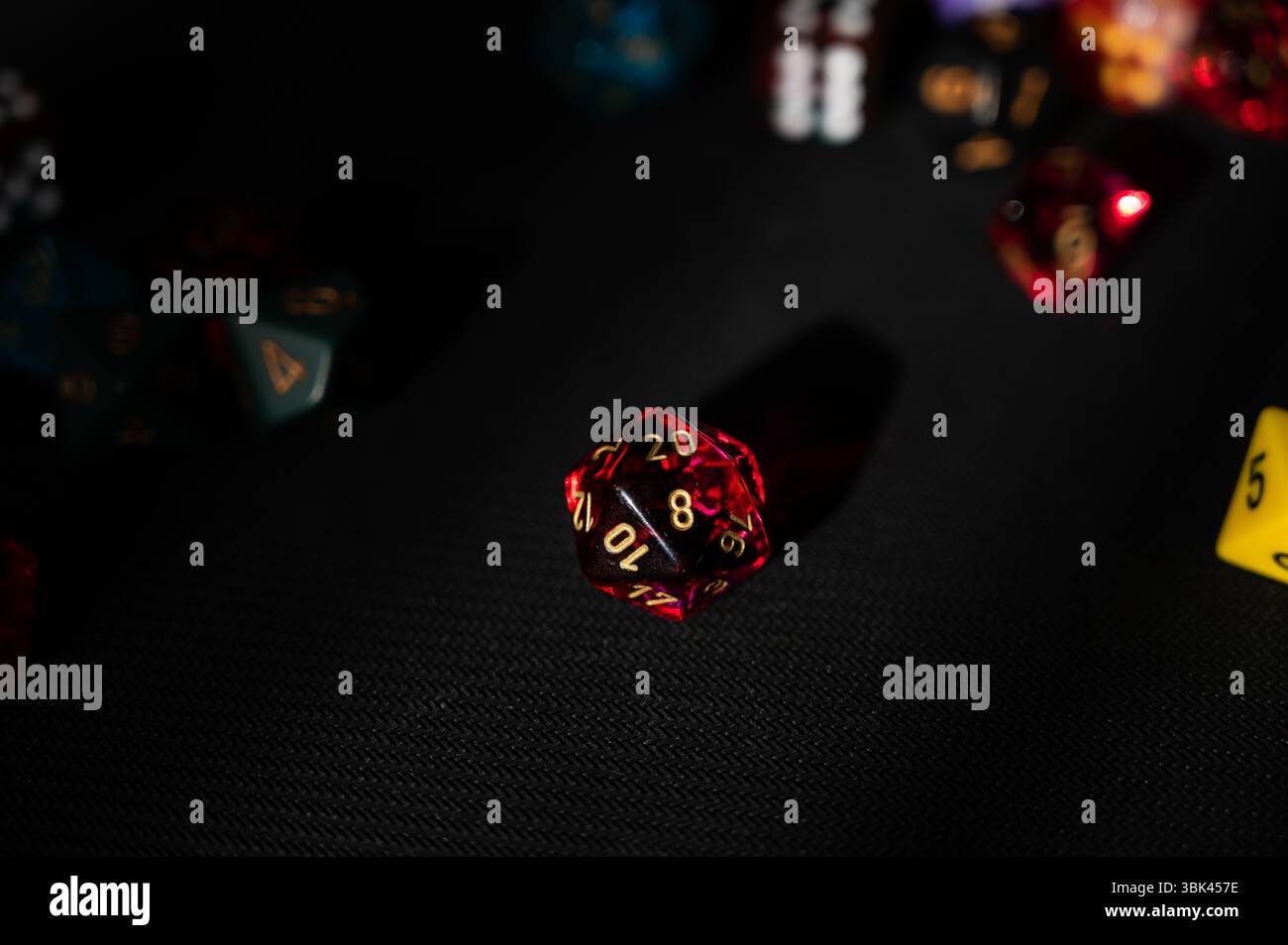 A dramatic, low-key photo of a single translucent red 20-sided die (D20 ...
