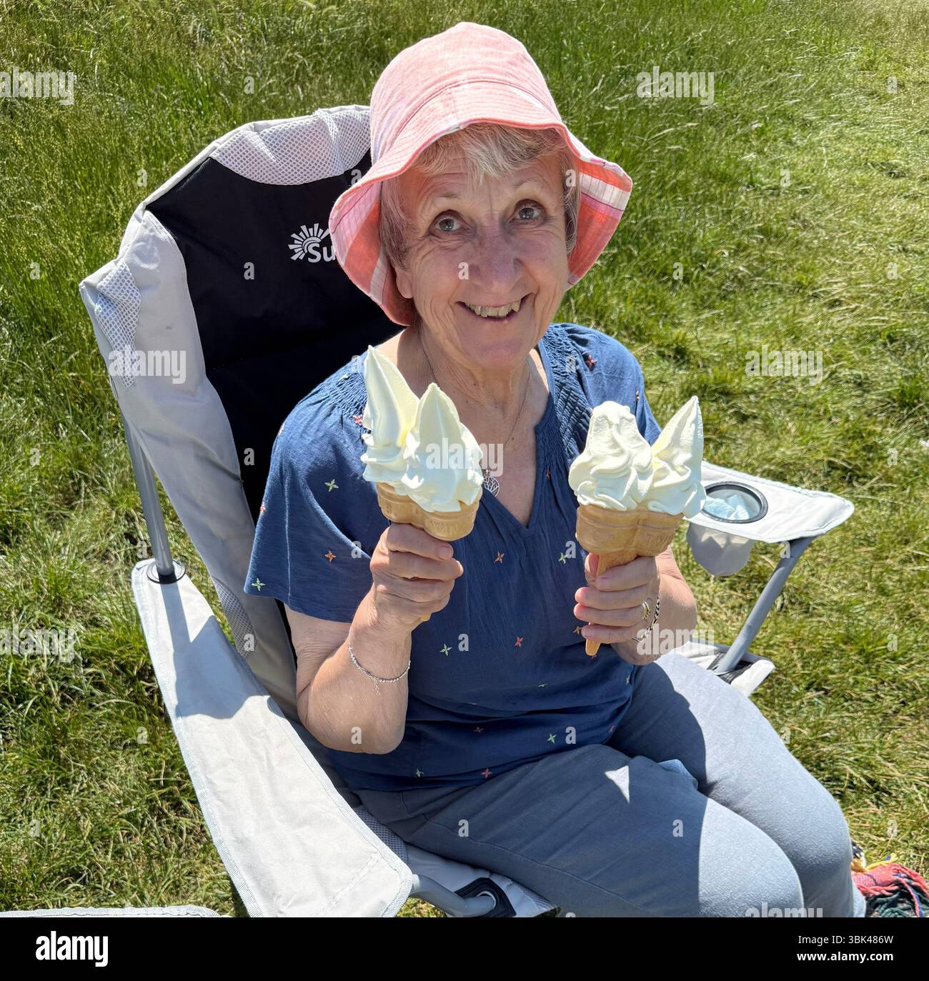 A retired, mature lady wearing a floppy hat, enjoying ice cream in Summer sunshine Stock Photo