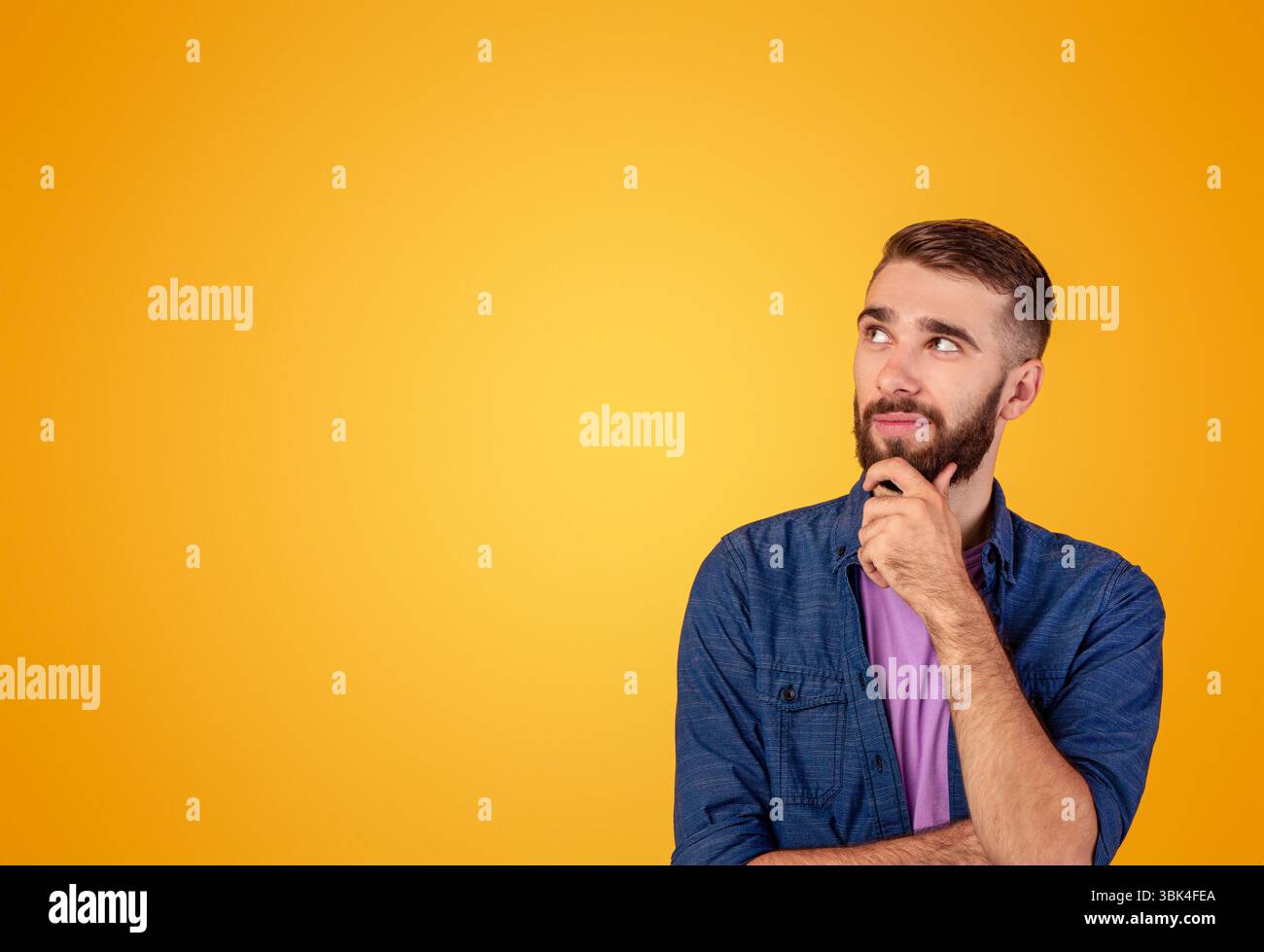 Dreamy hipster guy thinking over something, looking at empty space on orange studio background Stock Photo