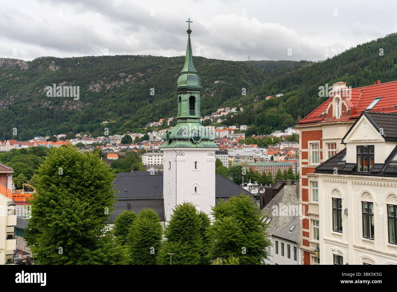 Historic church tower and rooftops with green mountain backdrop in ...