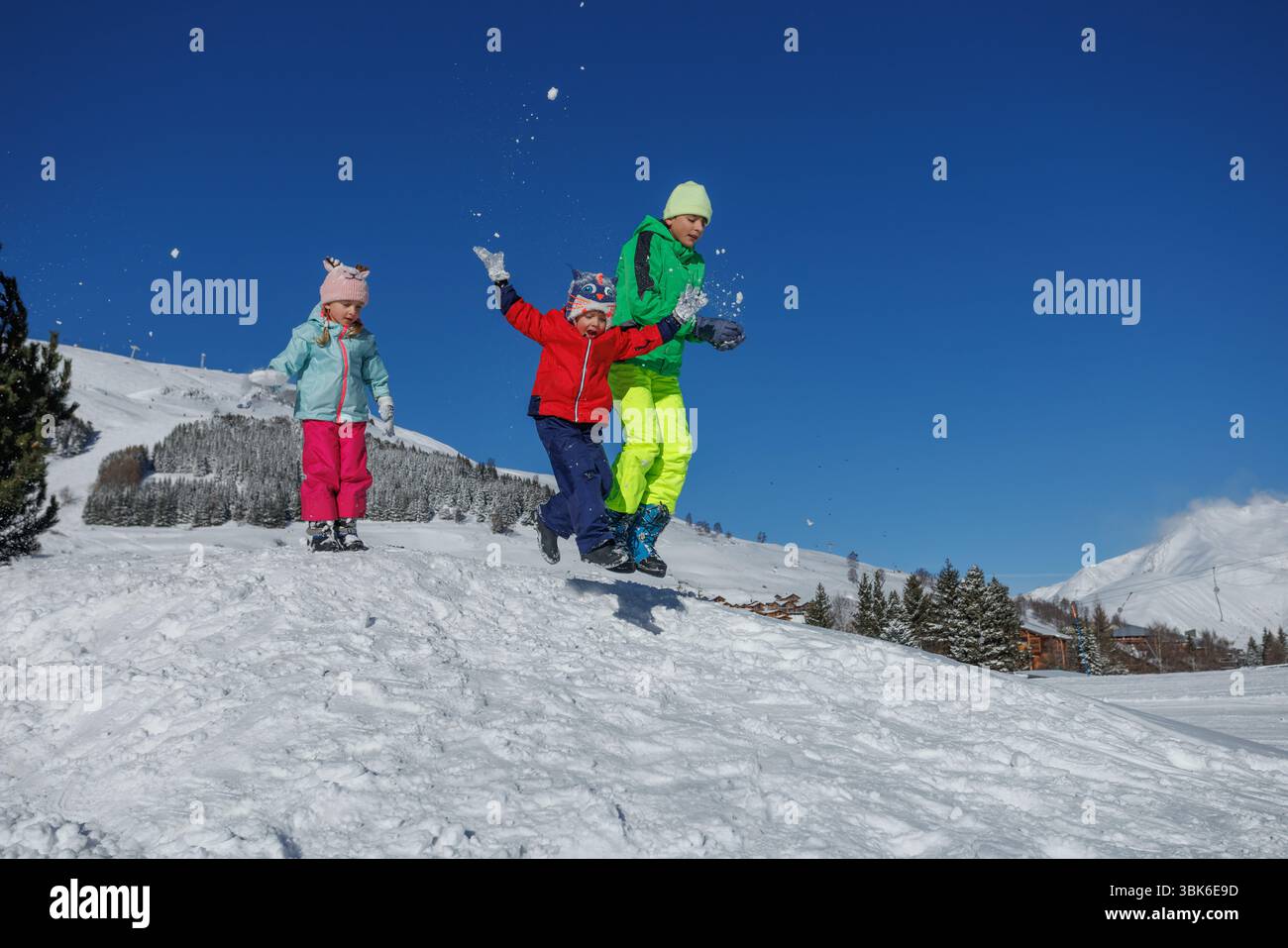 Snowy Fun Three kids in colorful winter gear jumping and having snowy fun Stock ...