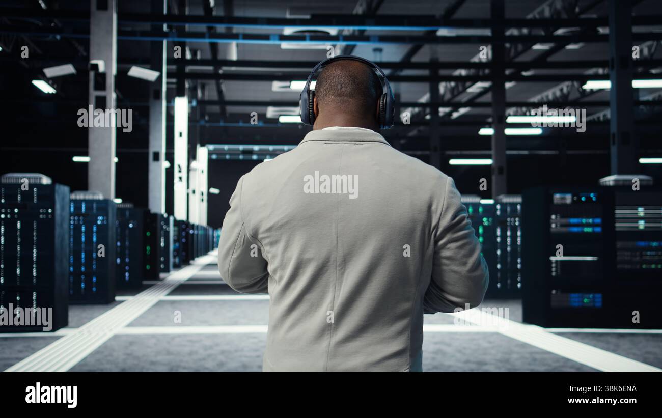 Admin walking in data center, listening music while doing inspection on infrastructure tech. IT specialist in server hub wearing headphones analyzing traffic patterns of equipment mainframes, camera A Stock Photo