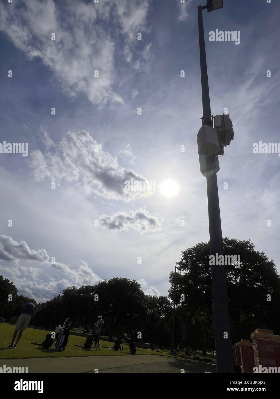 A sunny day at a golf course with lush green grass. Golfers prepare for their game under a bright, partly cloudy sky. - Smartphone Captured Stock Image