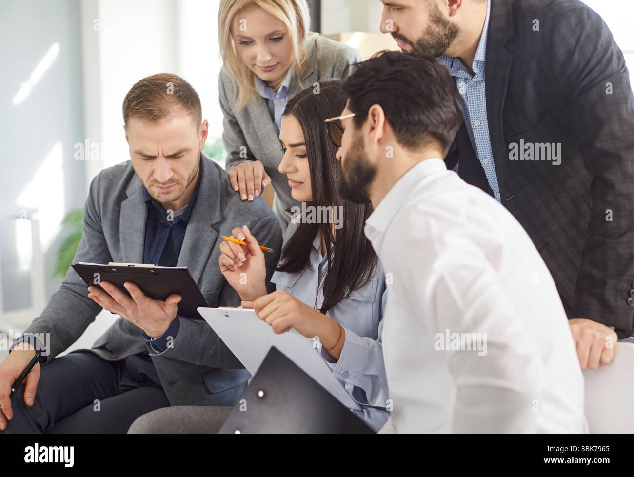 Focused business team gathered around tablet with documents discussing strategy and analyzing data. Stock Photo