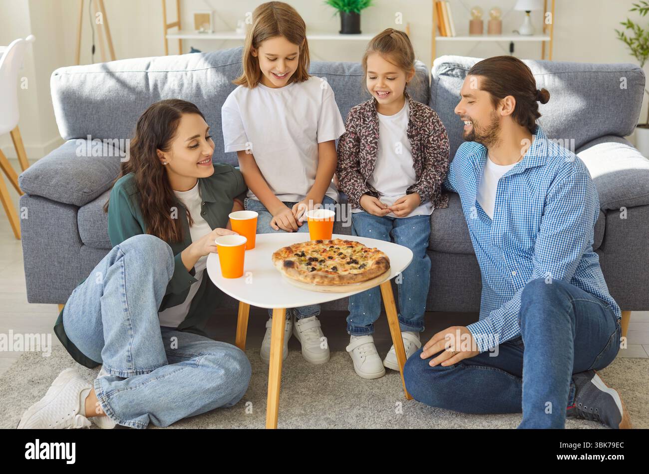Happy smiling family sitting around coffee table, sharing hot pizza and ...