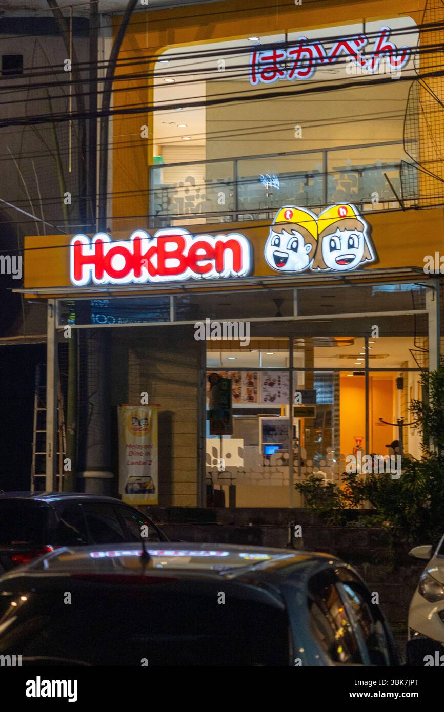 Bali, Indonesia - Dec 25, 2024: Neon sign for a restaurant called HOKBEN. The sign is lit up and has two cartoon faces on it. The restaurant is locate Stock Photo