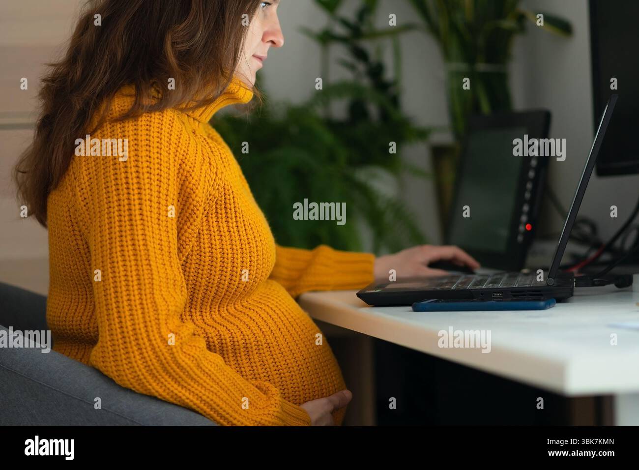 Pregnant woman working diligently on laptop, capturing the challenge of ...