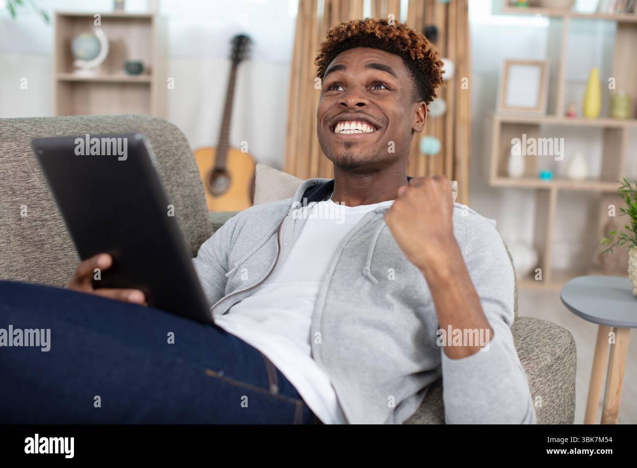 man with tablet in the living room celebrating a victory Stock Photo
