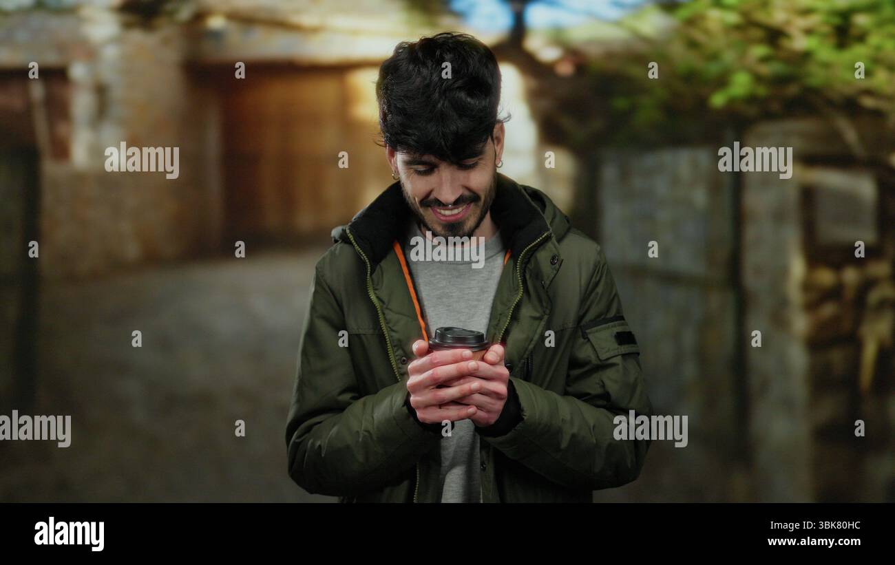 Young man in urban setting holding coffee cup, dressed warmly outdoors, showcasing style and warmth on a city street. Stock Photo