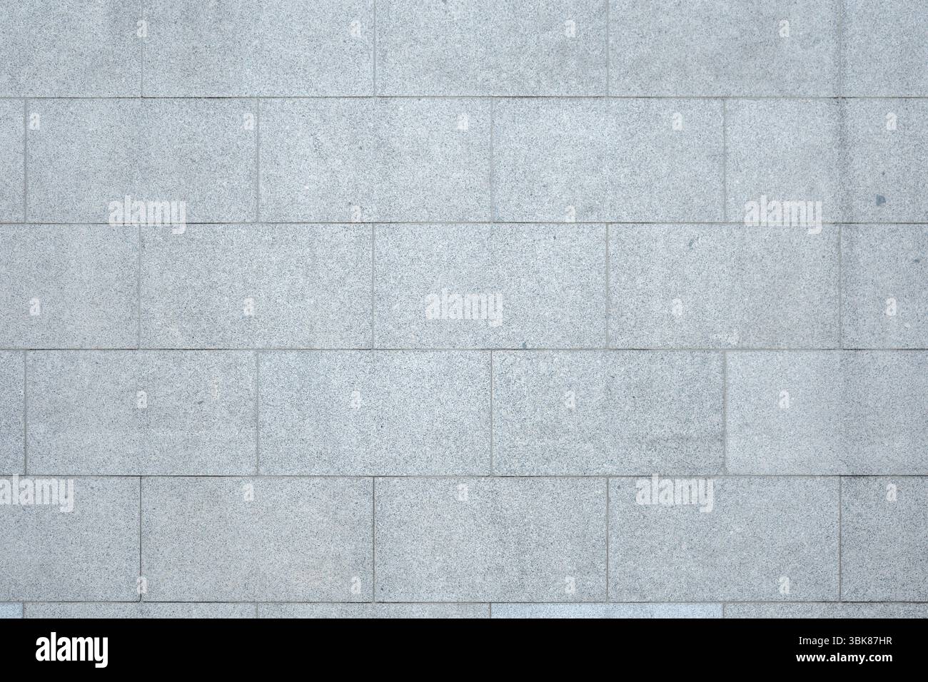 A full-frame, detailed view of a wall constructed from rectangular, light gray granite tiles. Stock Photo
