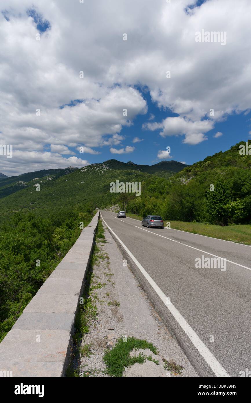 A winding road carves through lush green mountains under a bright ...
