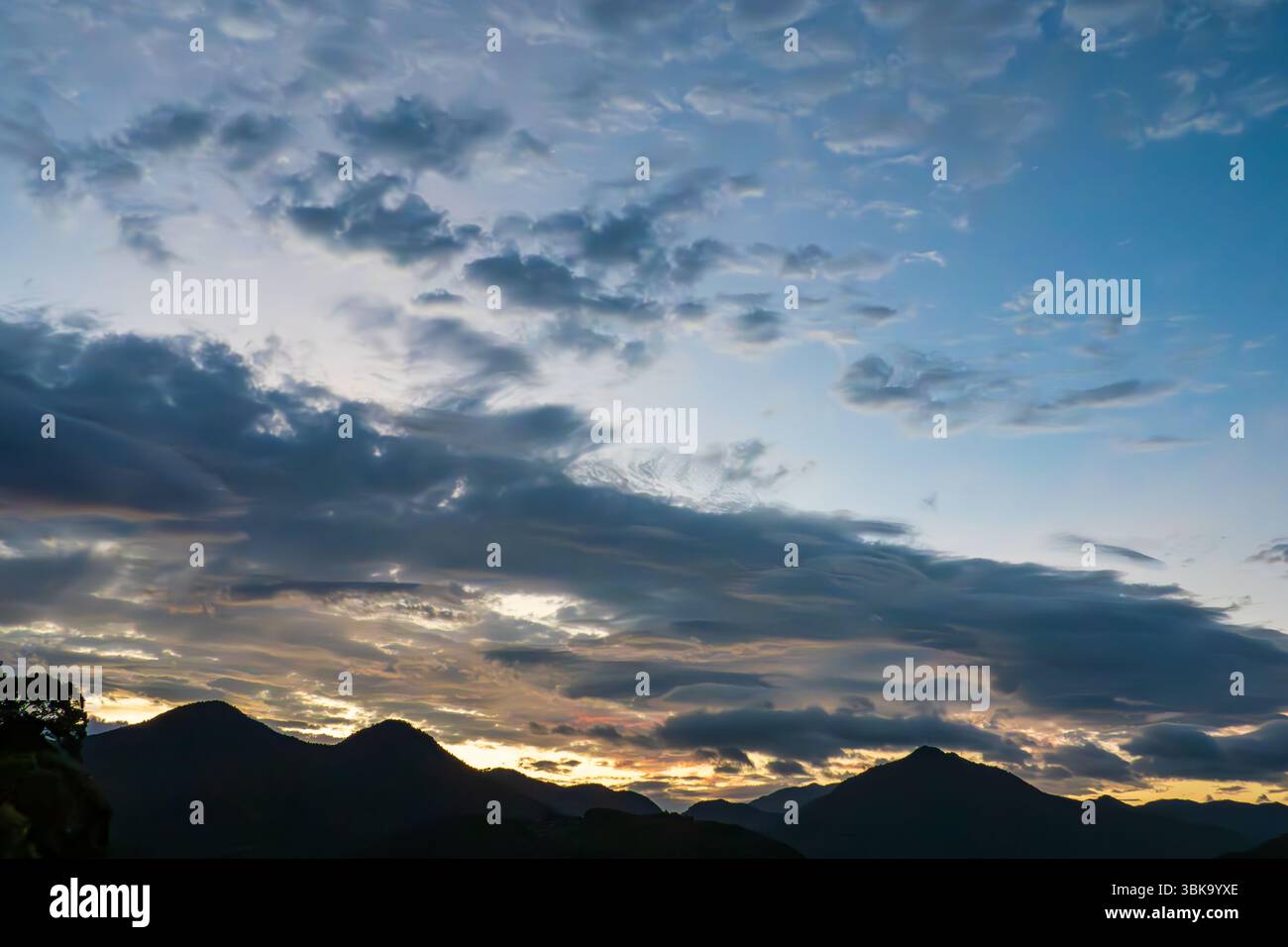 Dramatic Sunrise Over Mountain Silhouettes Beneath Dynamic Cloudscape Stock Photo