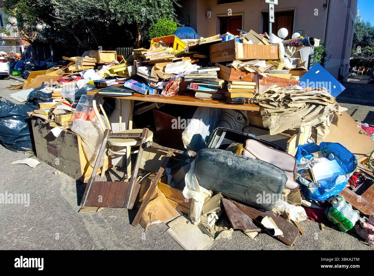 Large Pile Of Debris Including Damaged Furniture, Books, Personal Belongings, And Garbage Bags Sits On The Street In Front Of A Residential Building A Stock Photo