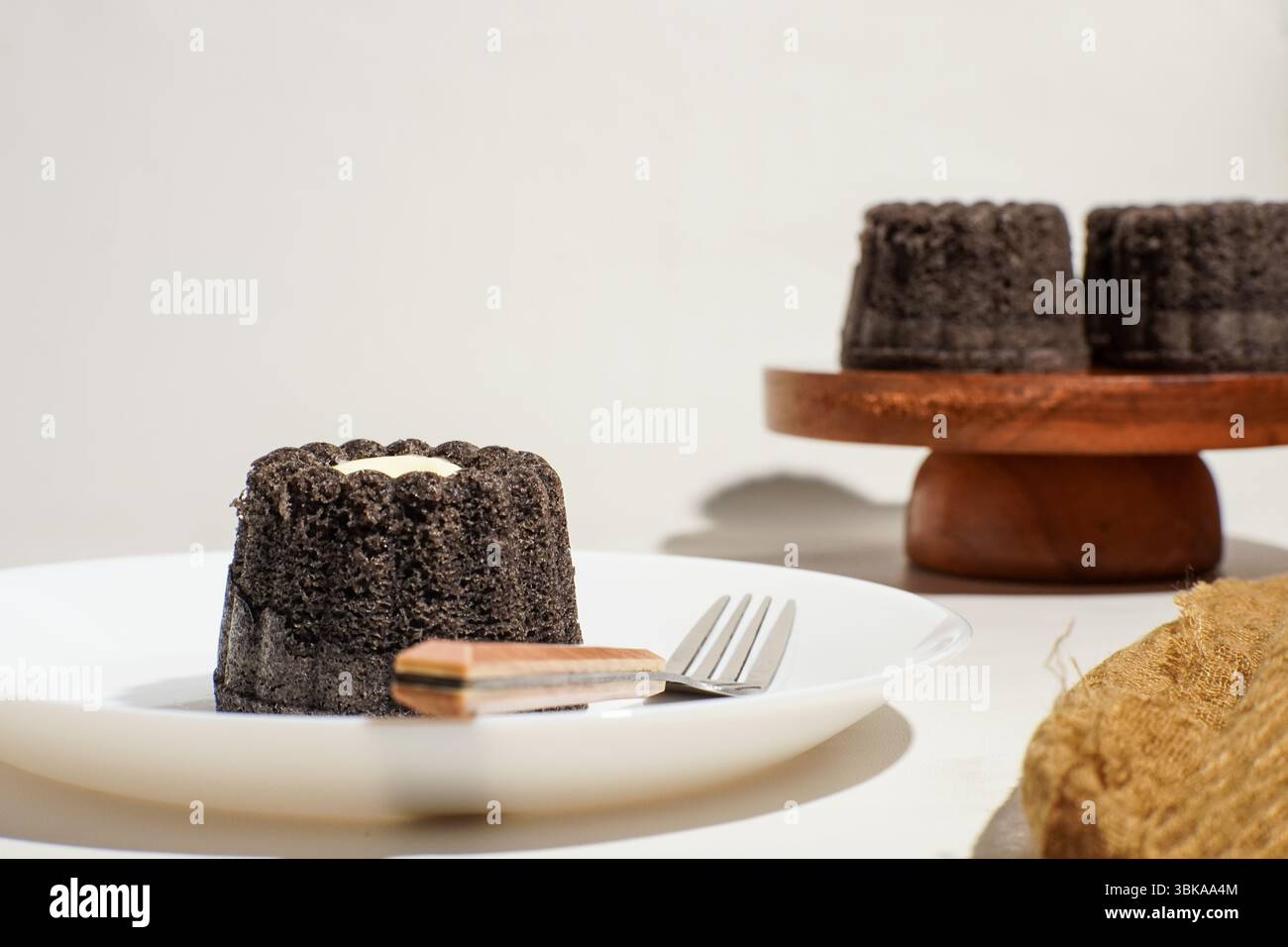 A single portion of black glutinous rice bundt cake with cheese center, placed on a ceramic plate with fork and spoon. Classic homemade dessert Stock Photo