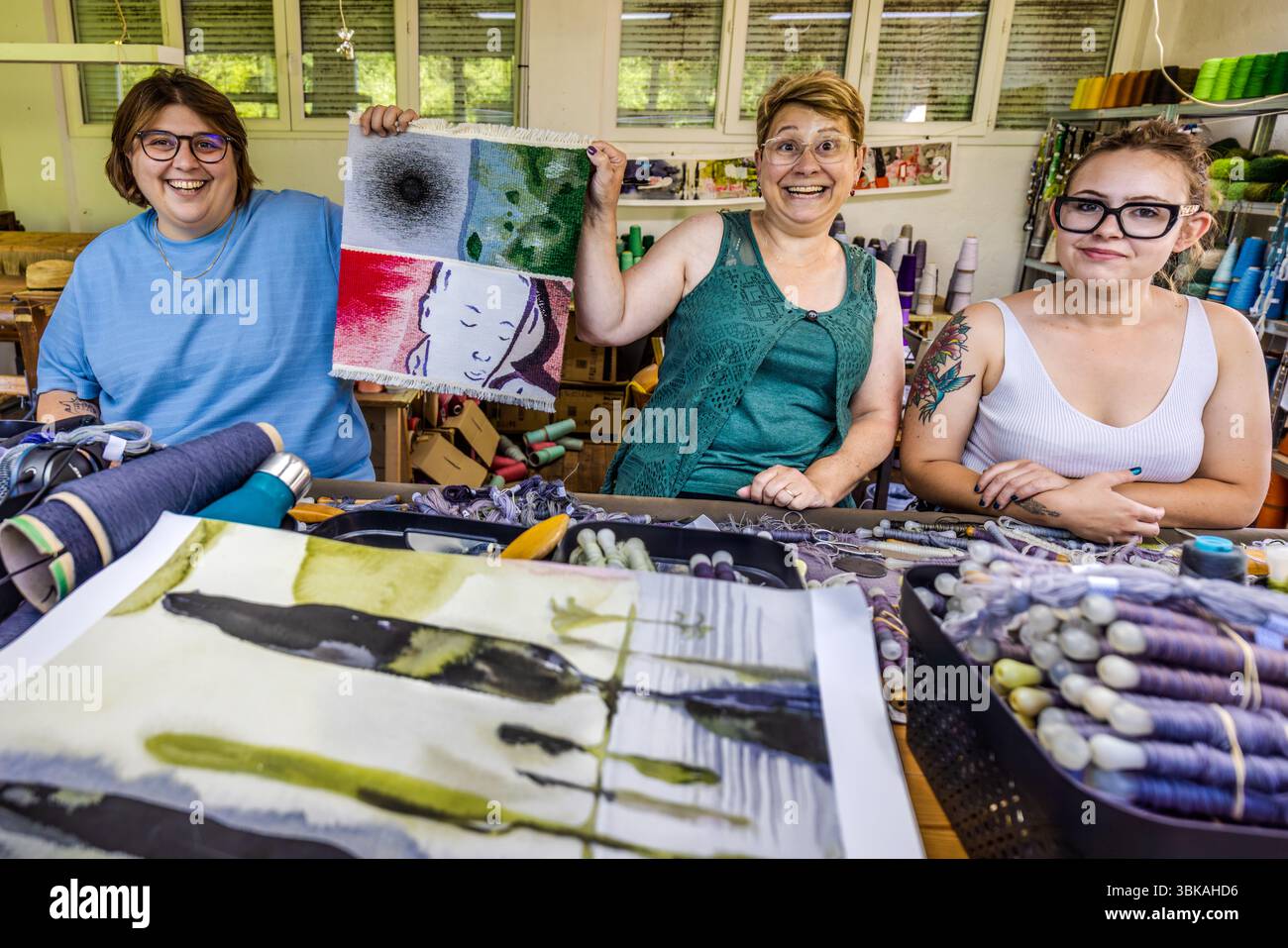 Sarah Chassain, team leader for the tapestry project "Hommage à George Sand" at the Robert Four studio with her colleagues Frederique and Agathe. They are holding up the sample piece they used to apply for the tender. The sample piece shows, in a small area, the various skills that a team must master in order to create the tapestry. Rue Madeleine, Aubusson, Nouvelle-Aquitaine, France Stock Photo