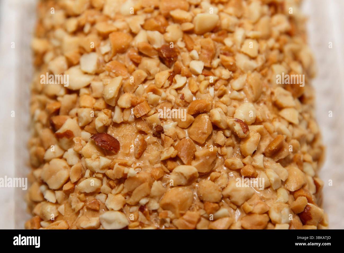 Crunchy crushed peanut texture covering a dessert surface, captured in close-up on a soft neutral background for sweet culinary concept Stock Photo