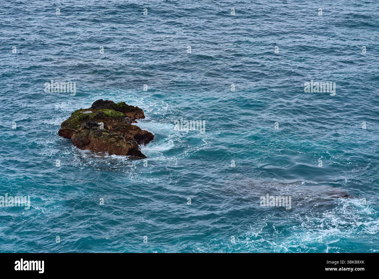 Aerial view of volcanic rock formations and ocean waves near El Bollullo beach in Tenerife, with foamy surf crashing against dark boulders and mossy s Stock Photo