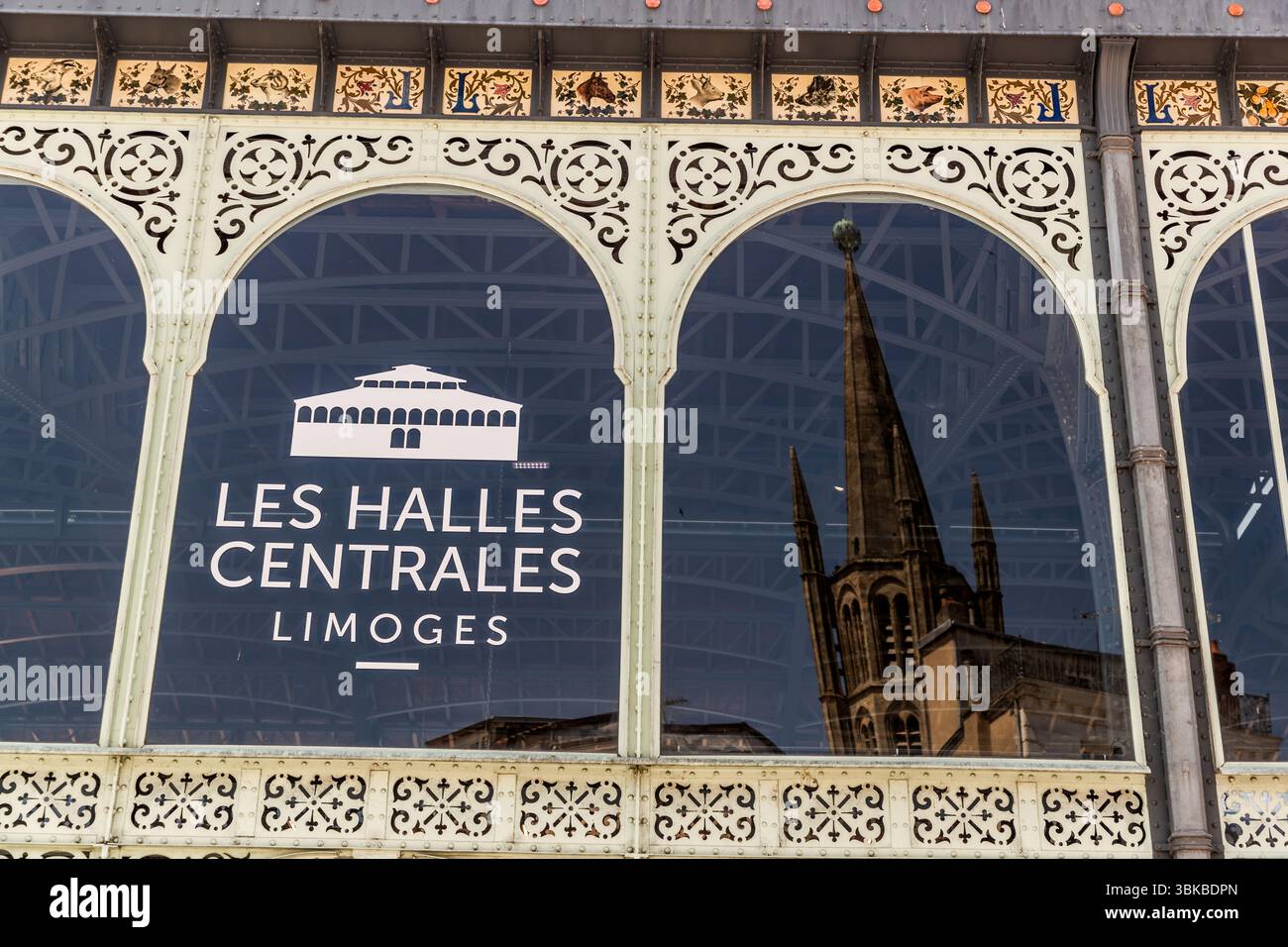 Window of the Limoges market hall with reflection of the cathedral. The Limoges market hall, known as the Halles centrales, has been a listed monument since 1976 and is particularly impressive due to its surrounding porcelain frieze with 368 tiles depicting flowers, birds and market hall products. Place Saint-Michel, Limoges, Nouvelle-Aquitaine, France Stock Photo